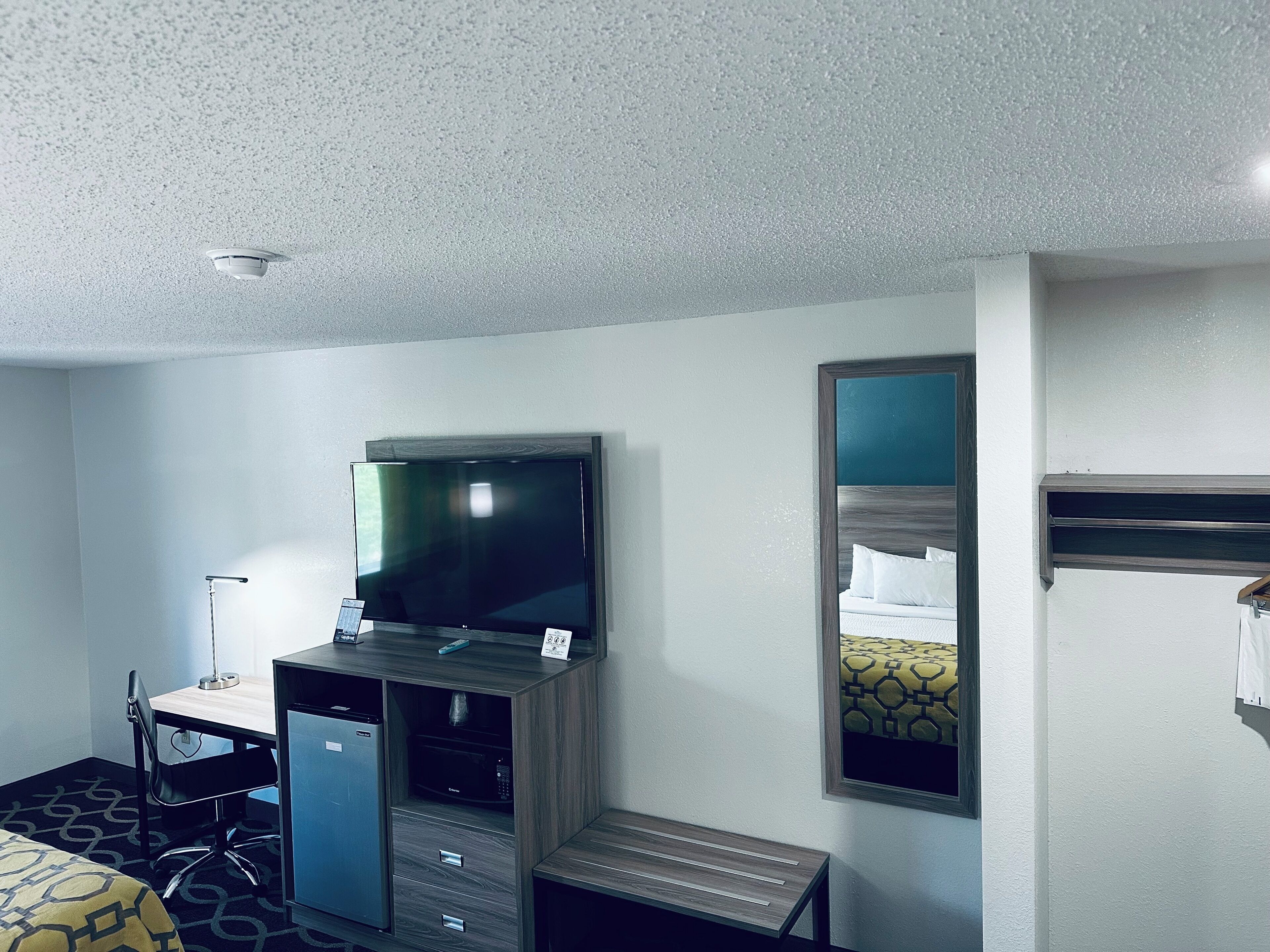 A hotel room with a bed, a desk with a computer, a television, a mirror, and a bunk bed.