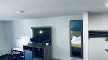 A hotel room with a bed, a desk with a computer, a television, a mirror, and a bunk bed.