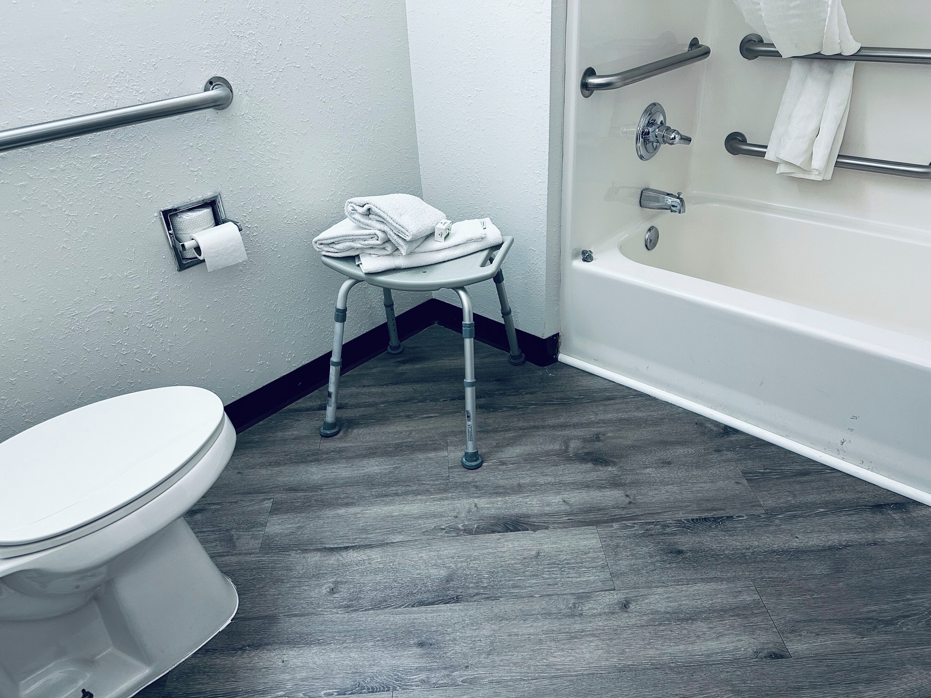 A bathroom with a toilet, a small step stool with towels, a grab bar, and a bathtub.