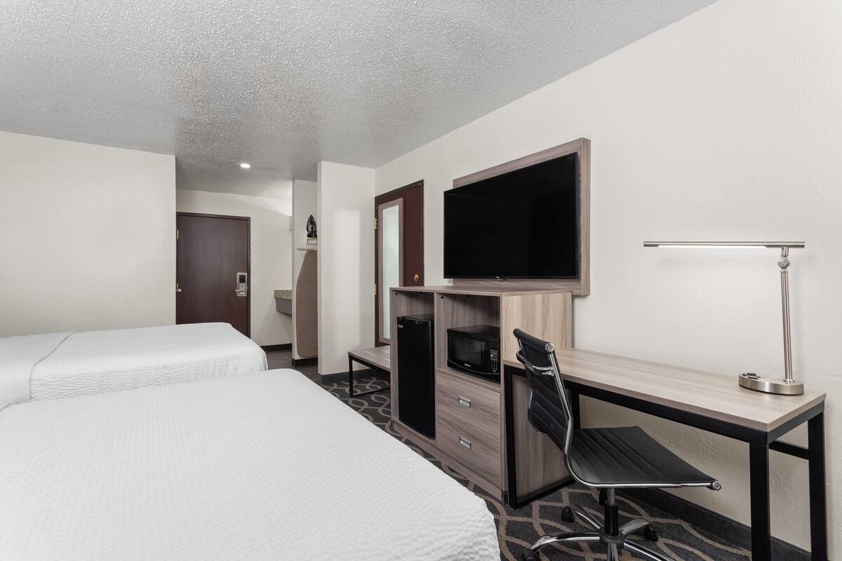 Habitación de hotel con dos camas, un escritorio con silla, un televisor de pantalla plana, un microondas y una lámpara.