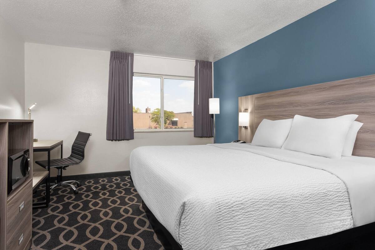Habitación de hotel con cama, escritorio, silla y ventana con cortinas.