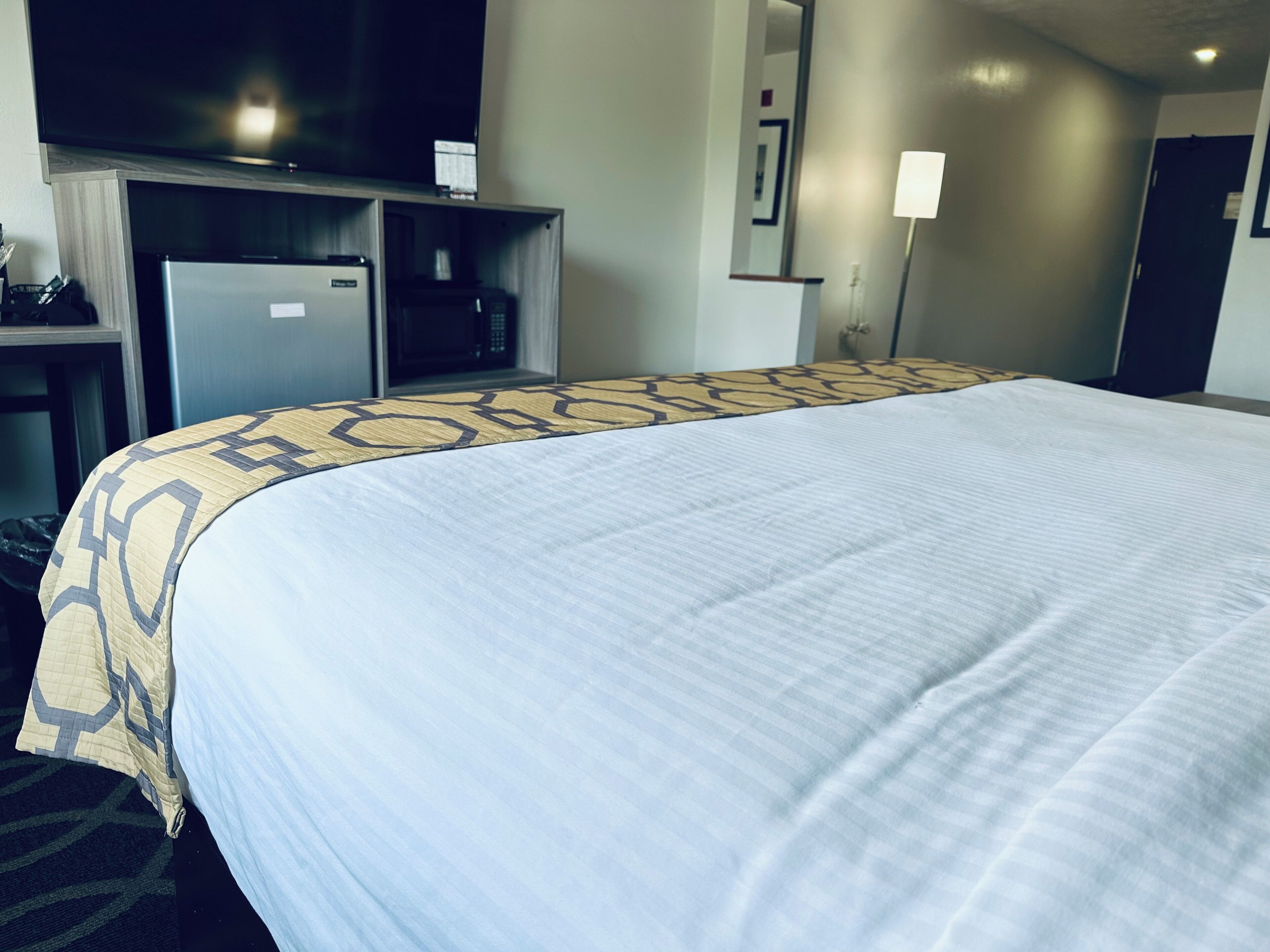 Habitación de hotel con una cama grande, un escritorio con microondas y un televisor encima.