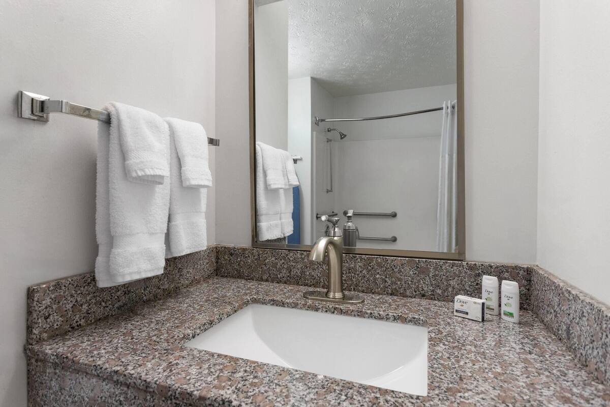Un baño con lavamanos de encimera de granito, un espejo y dos jabones Dove.