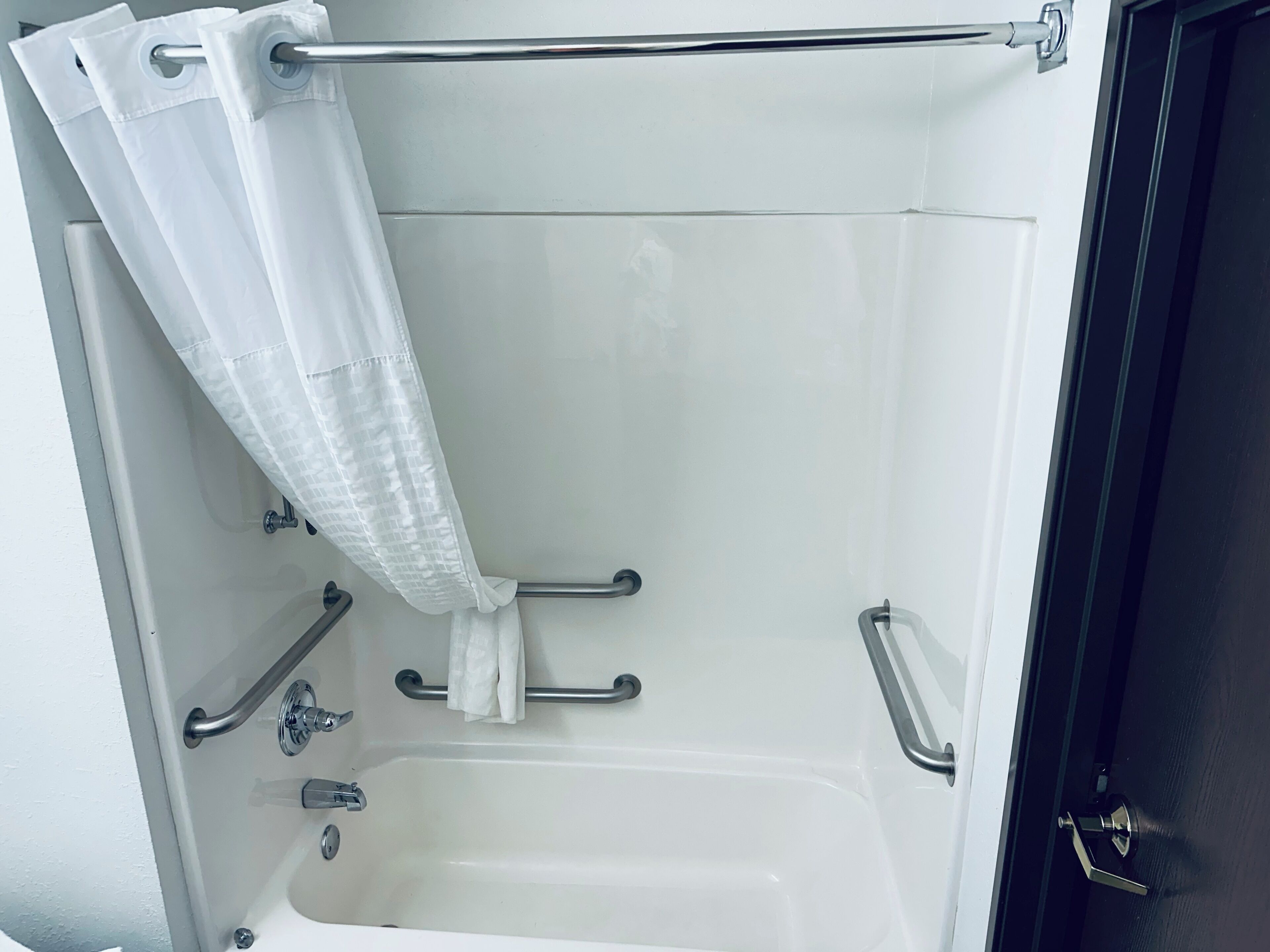 Eine Badewanne mit Duschvorhang, Haltegriffen und einem Handtuchhalter.