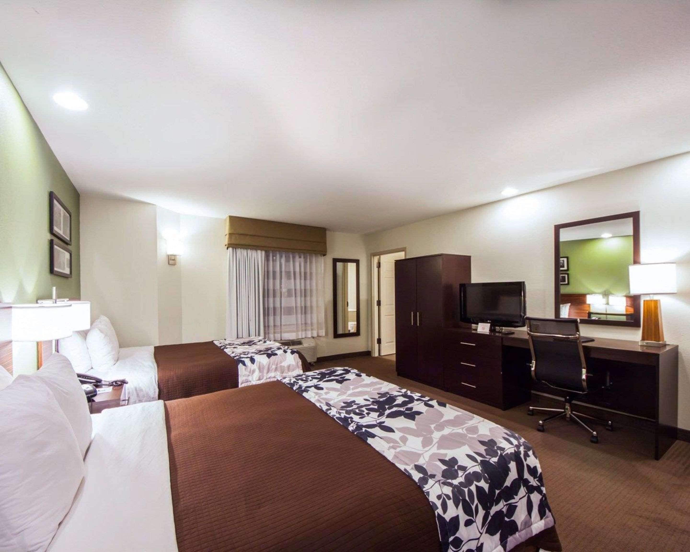 Habitación de hotel con dos camas, un escritorio con una computadora, un televisor y un espejo.