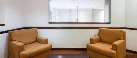 A room with two beige armchairs, a dark wooden coffee table, and a large mirror on the wall.