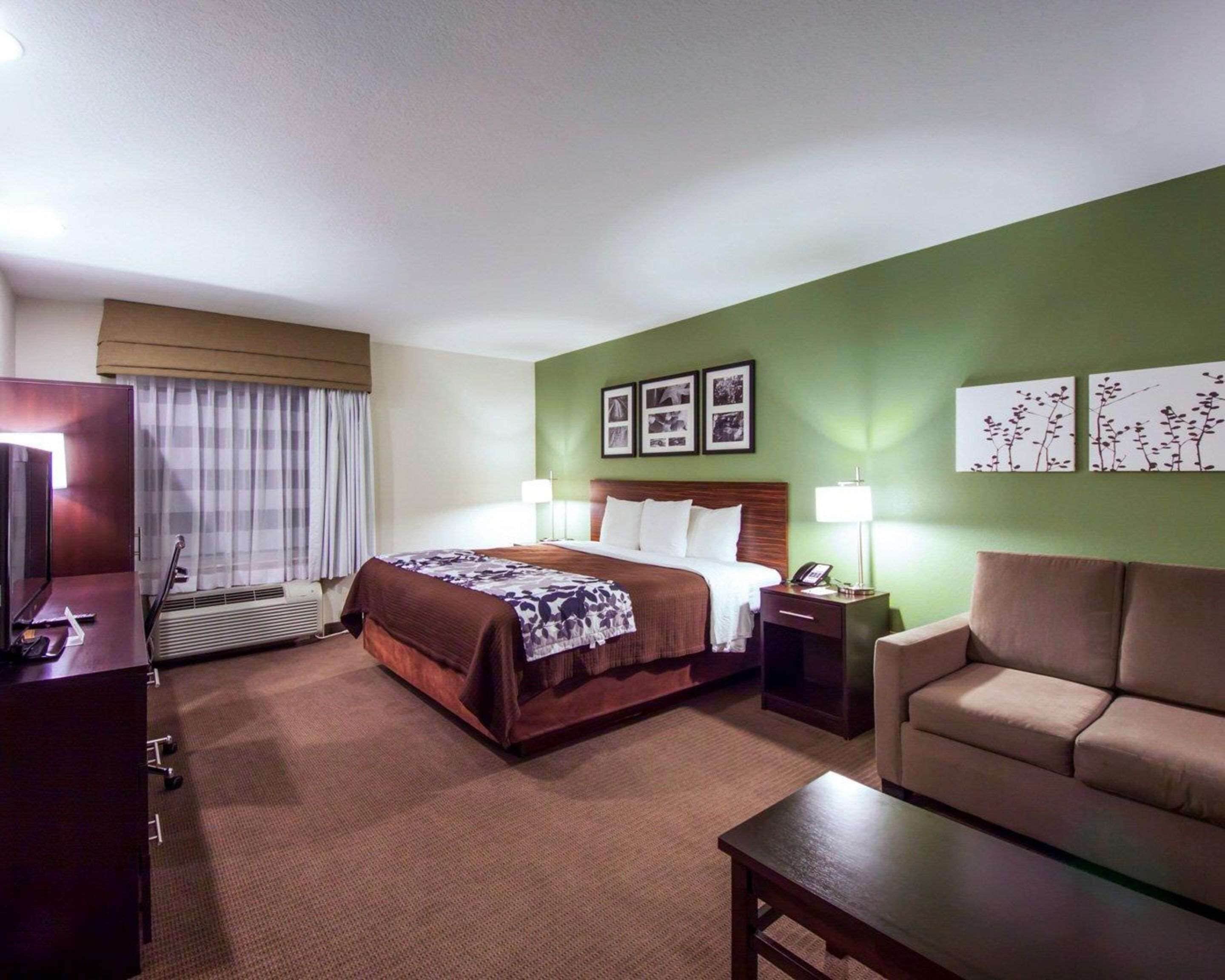 Une chambre d’hôtel avec un lit, une table de chevet, une lampe et un canapé.