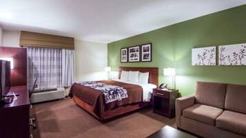 A hotel room with a bed, bedside table, lamp, and a sofa.