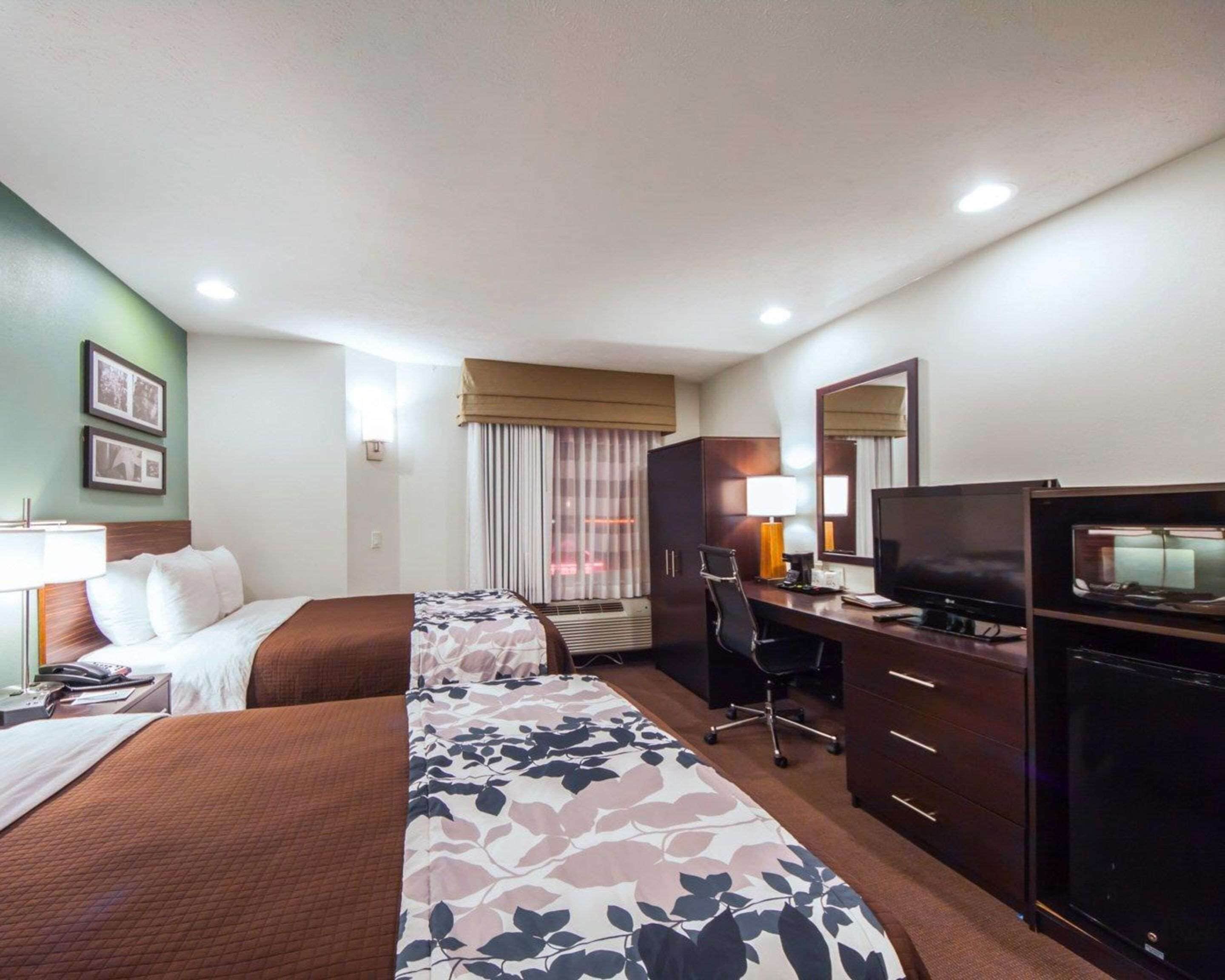 A hotel room with two beds, a desk, a television, and a dresser.