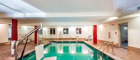 An indoor swimming pool with a tiled floor, a pool ladder, and a few lounge chairs.