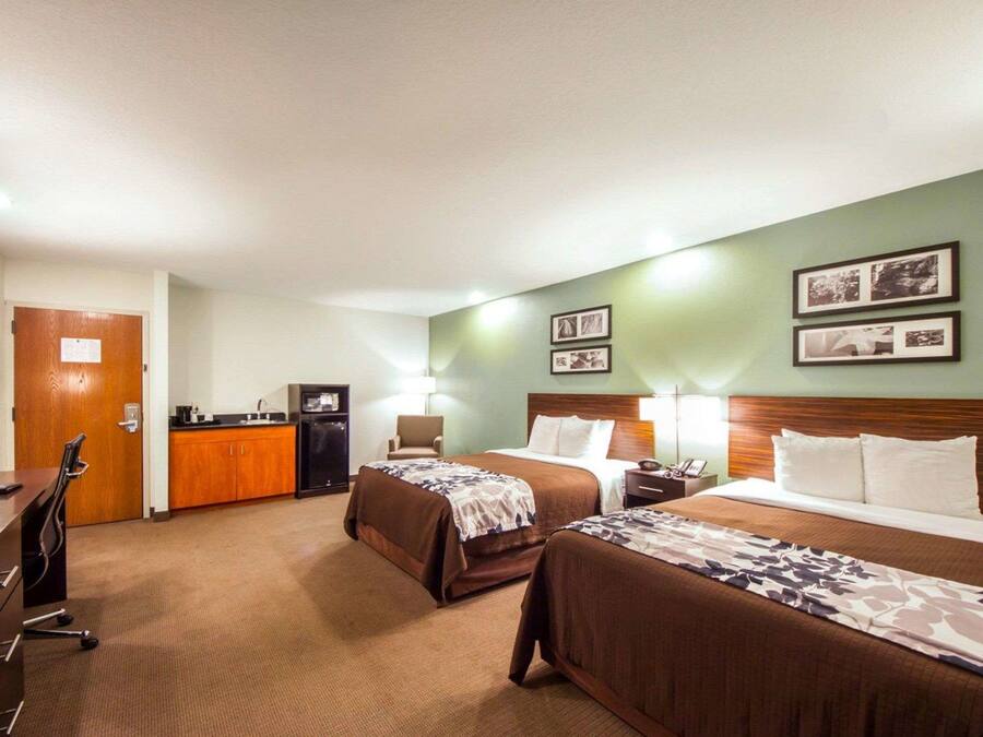 Habitación de hotel con dos camas, un escritorio con ordenador, una silla y una pequeña cocina.