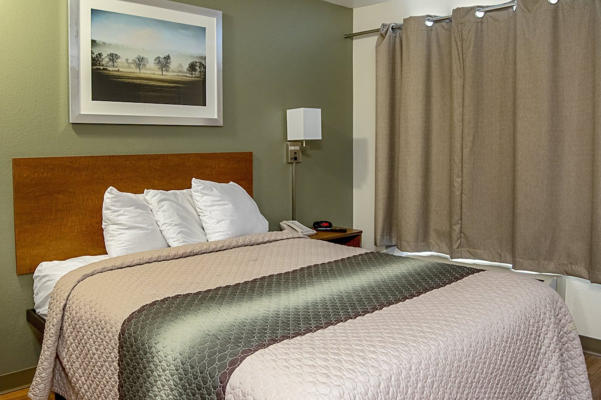 A neatly made bed with a headboard, a bedside table with a lamp, and a framed picture on the wall.