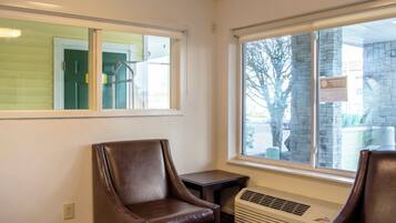 A room with two leather chairs, a small table, a window with a view of a building and trees, and a wall-mounted air conditioning unit.