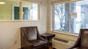 Una habitación con dos sillones de cuero marrón, una mesita, un ventanal con vistas a un edificio y árboles, y un conducto de ventilación en la pared.