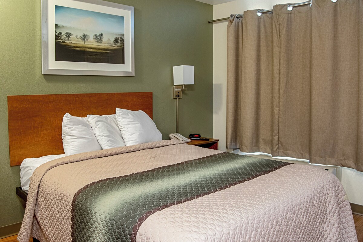 Habitación de hotel con cama, mesita de noche con lámpara, teléfono y un cuadro en la pared.