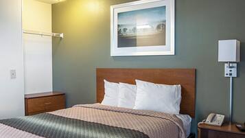 Habitación de hotel con cama, mesita de noche con teléfono, lámpara de pared e imagen en un marco.
