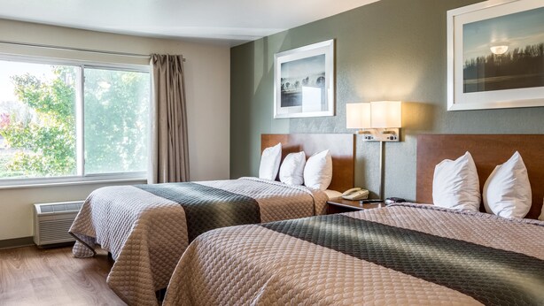 Habitación de hotel con dos camas, un ventanal con cortinas, un teléfono en la pared y cuadros enmarcados.