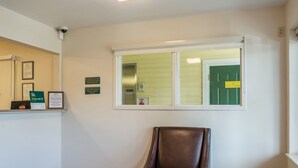 Una habitación con un sillón de cuero marrón, una recepción con diplomas enmarcados y una ventana con vista a una puerta verde.