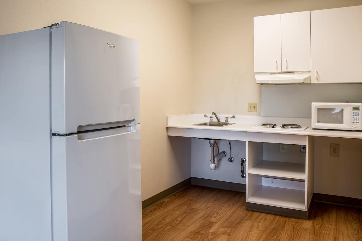 A compact kitchen with a white refrigerator, a microwave, and white cabinets.