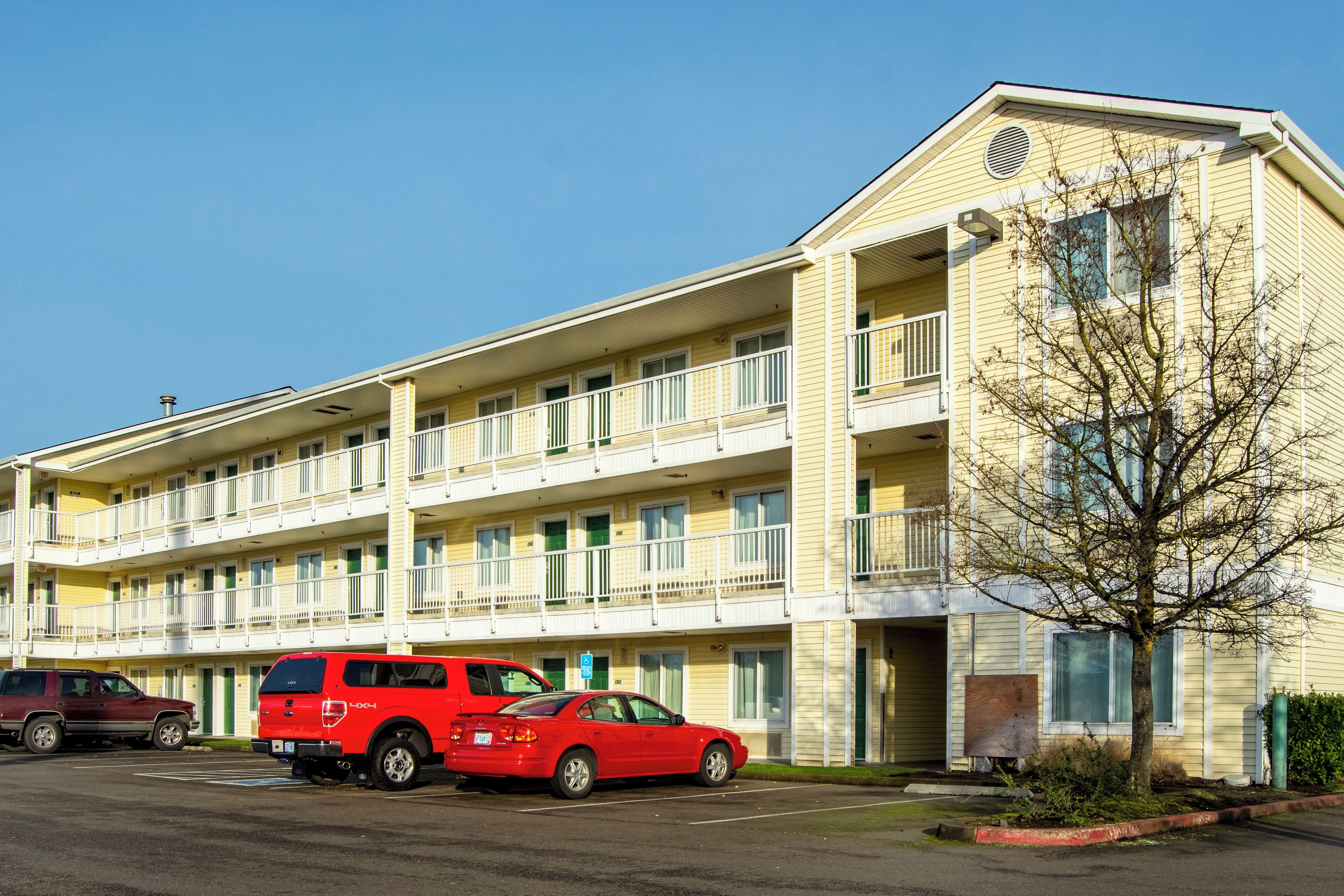 A multi-story hotel with a parking lot, featuring a red SUV and a sedan.