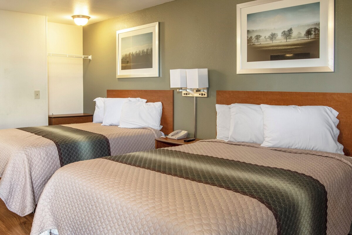 Habitación de hotel con dos camas, una mesita de noche con teléfono, lámpara y cuadros en la pared.