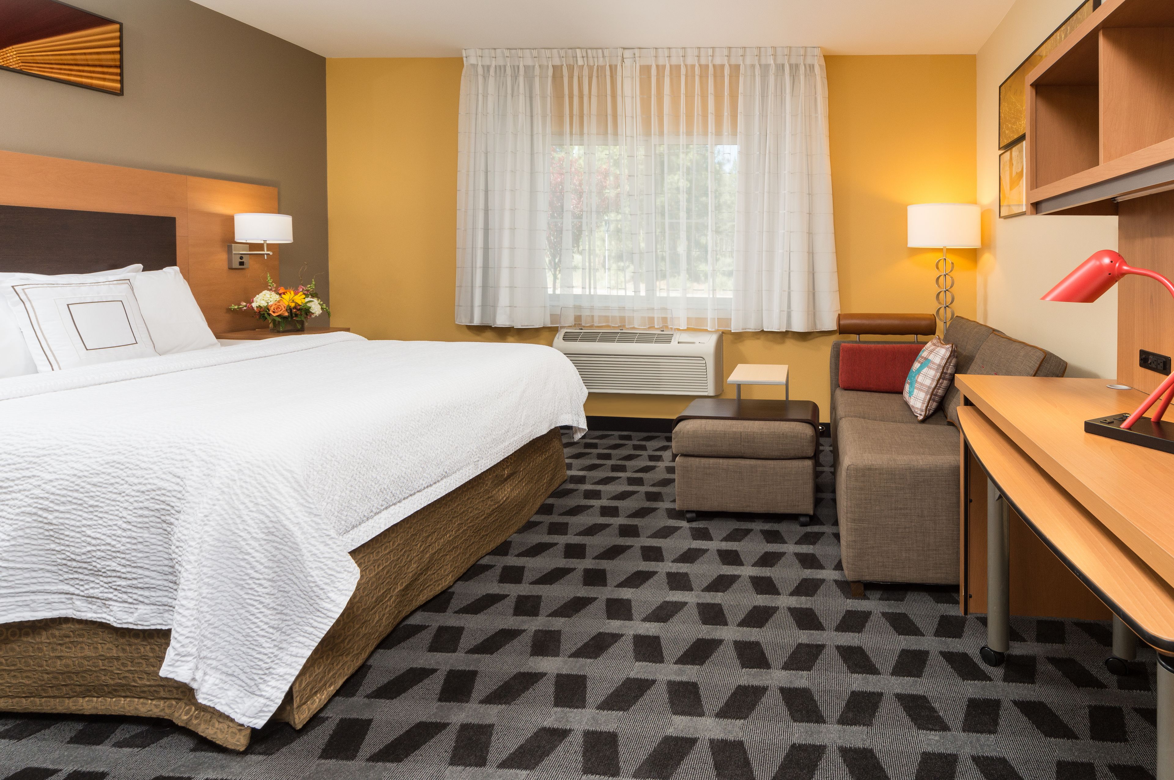 A hotel room with a large bed, a desk, a sofa, and a window with curtains.