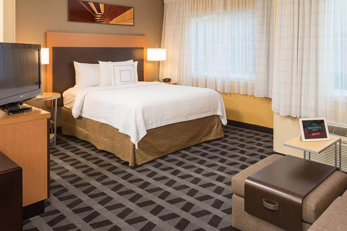 Une chambre d’hôtel avec un lit, une télévision, un bureau et une petite table sur laquelle est posé un panneau.