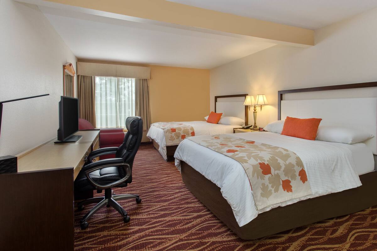 Ein Hotelzimmer mit zwei Betten, einem Schreibtisch mit Computer, einem Stuhl und einem Fernseher.