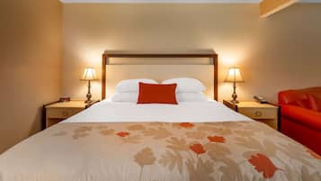 A hotel room with a large bed, two bedside tables, a red sofa, and a floral-patterned bedspread.