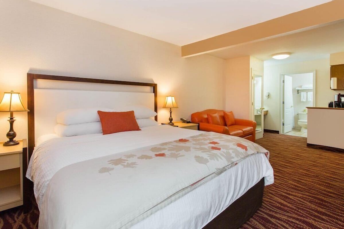 A hotel room with a large bed, two bedside lamps, an orange chair, and a desk with a mirror.