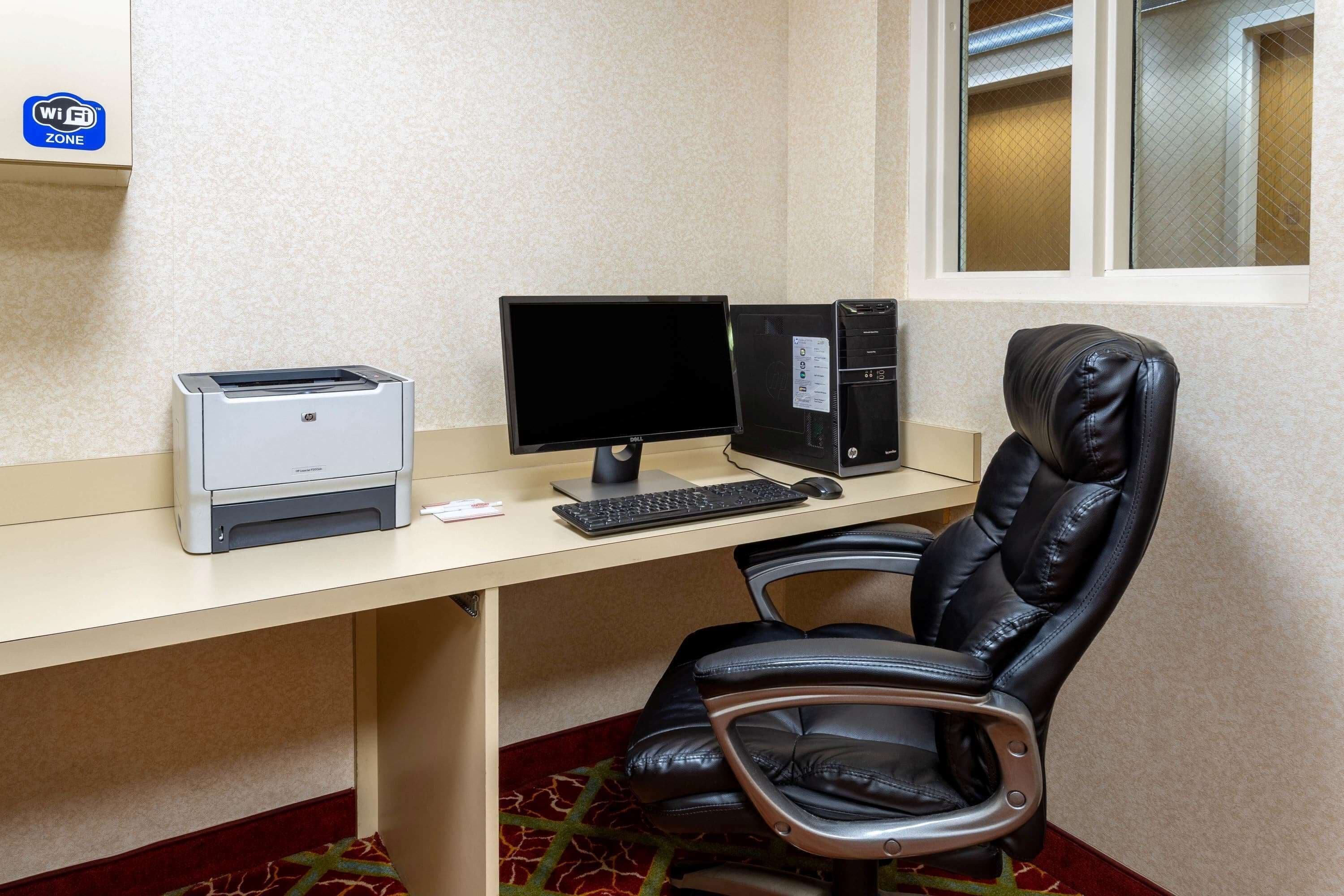 Una camera d'albergo con una scrivania, una stampante, un computer e una poltrona in pelle.