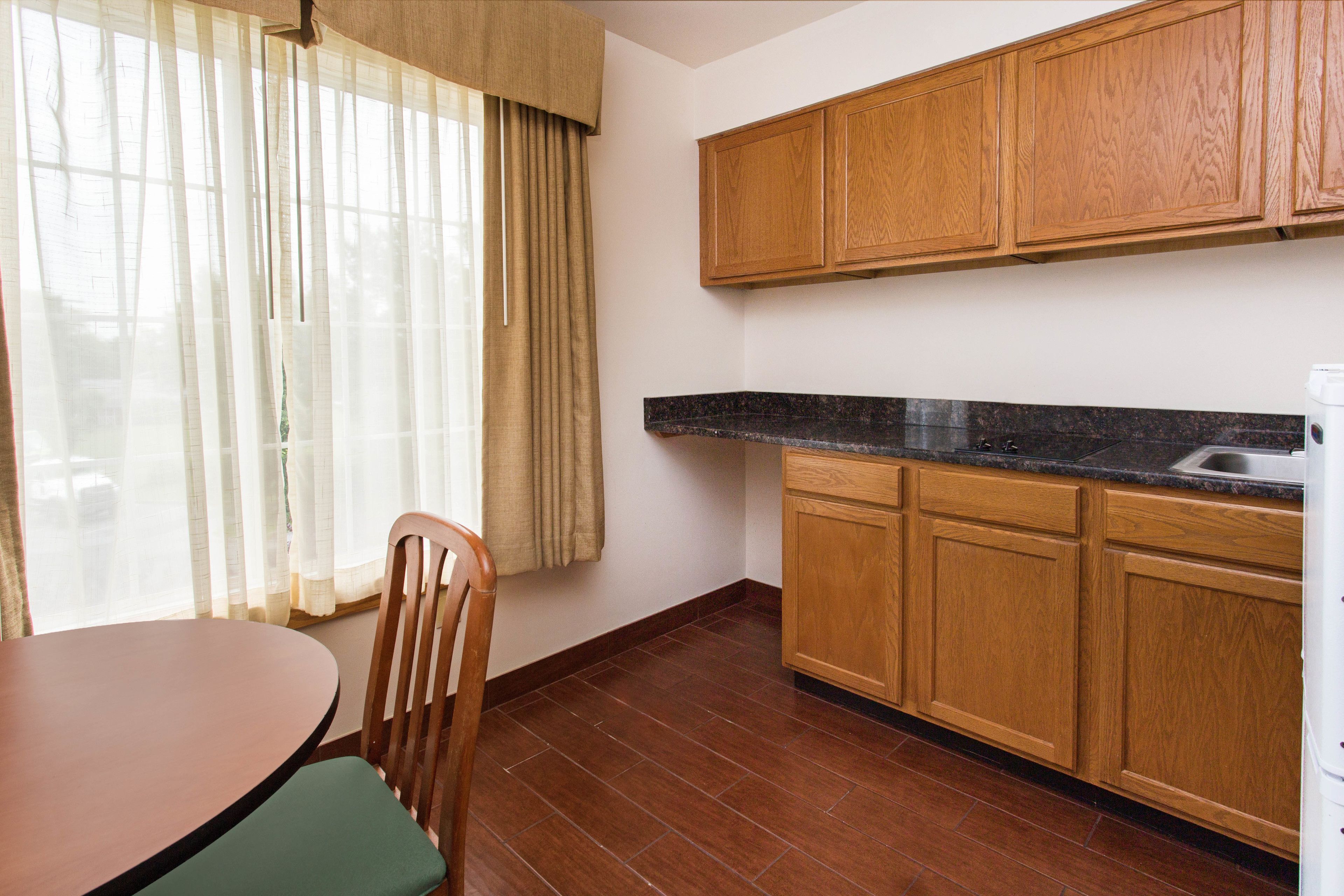 Una cocina con armarios de madera, encimera de granito y ventana con cortinas.