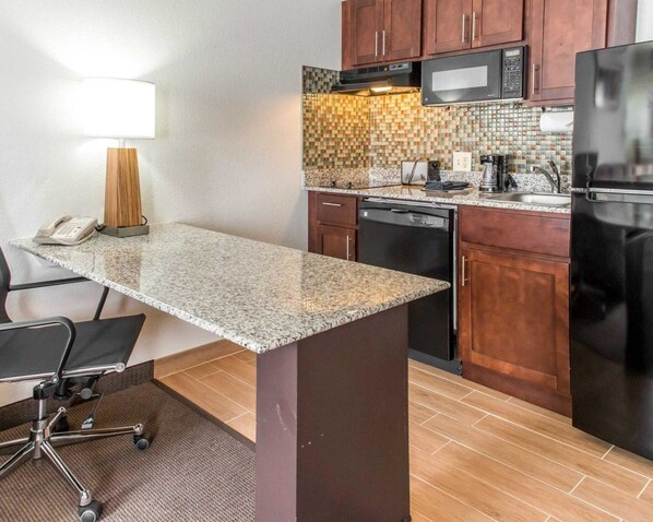 A compact kitchen with a granite countertop, wooden cabinets, a microwave, a refrigerator, and a dishwasher.