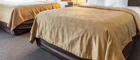 A hotel room with two beds, each with a headboard, a bedside table with a lamp, and a carpeted floor.