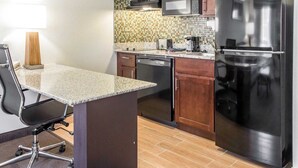 A compact kitchen with a granite countertop, a black refrigerator, wooden cabinets, a microwave, and a dishwasher. - MainStay Suites Pittsburgh Airport (Pittsburgh)