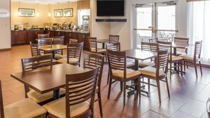 A dining area with multiple tables and chairs, a kitchen in the background, and a large TV mounted on the wall. - MainStay Suites Pittsburgh Airport (Pittsburgh)