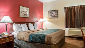 Habitación de hotel con una cama grande, dos lámparas de noche, una mesita de noche con teléfono y dos cuadros en las paredes.