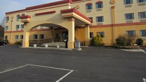 Un hotel de varios pisos con fachada roja y color beige, entrada cubierta y estacionamiento.