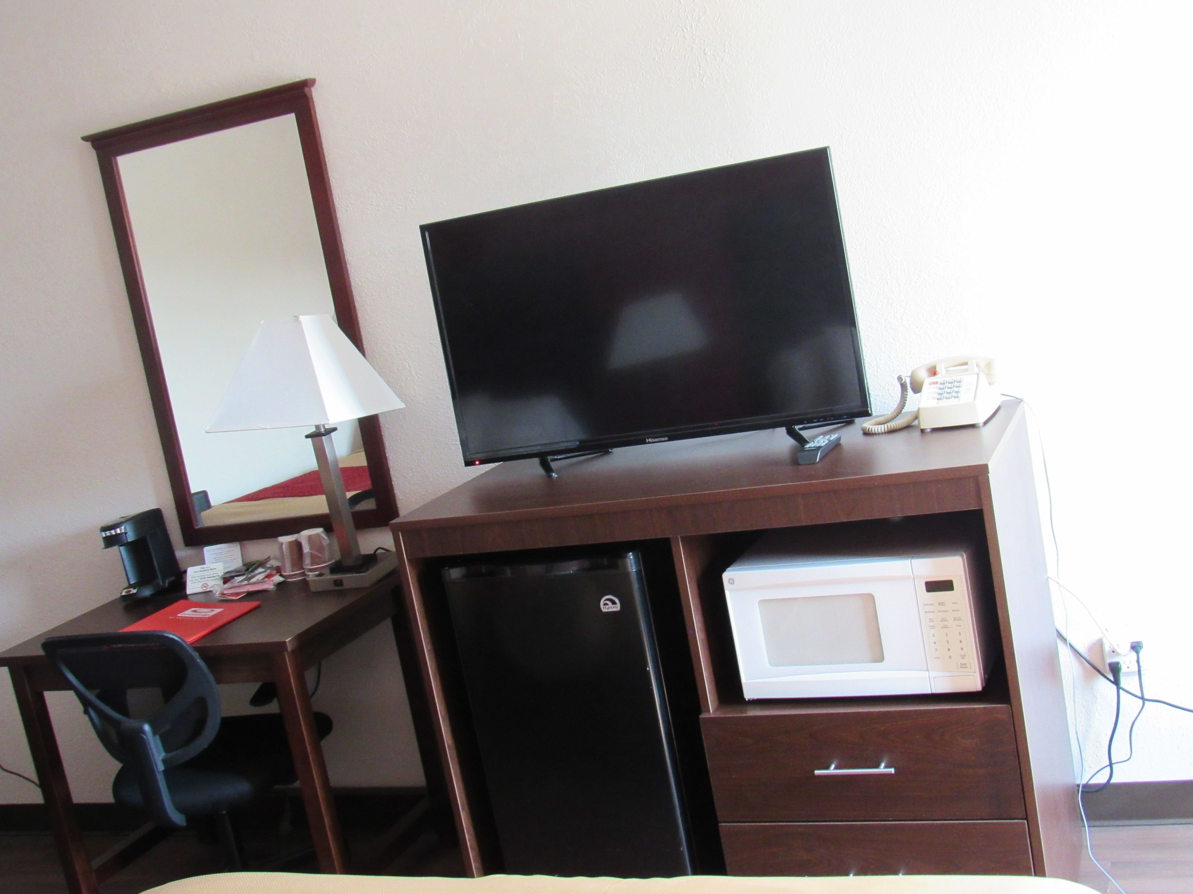Una habitación de hotel con escritorio, televisión, microondas y refrigerador.