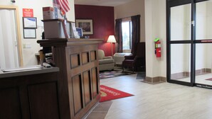Un área de recepción con un mostrador de madera, alfombra roja, un sofá y una ventana con cortinas.