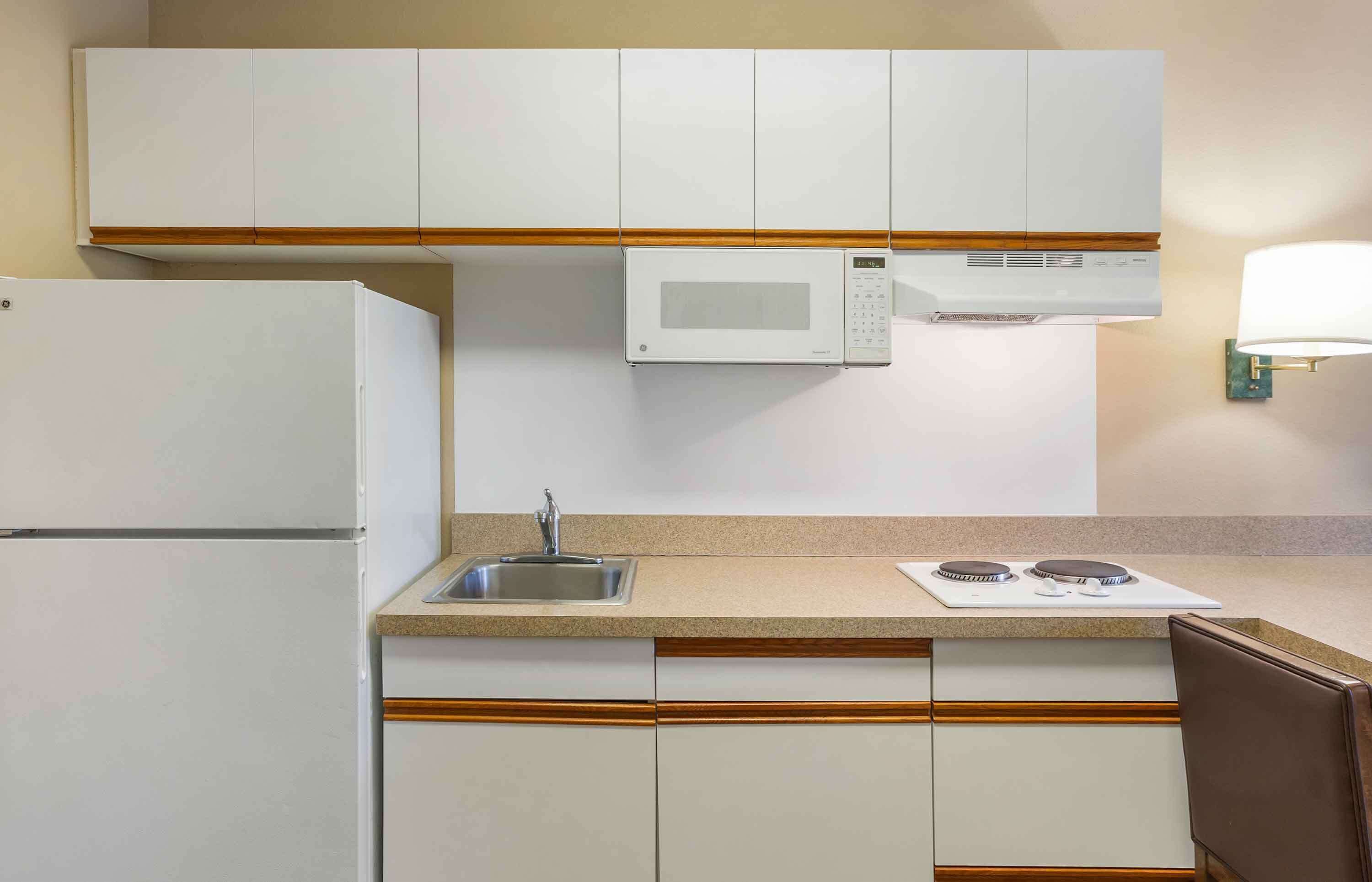 Una cocina compacta con armarios blancos, microondas, lavabo y estufa.