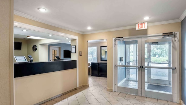 A hotel reception area with a reception desk, a digital screen, a clock, and an exit door. - Extended Stay America Suites Philadelphia Horsham Dresher Rd (Horsham)