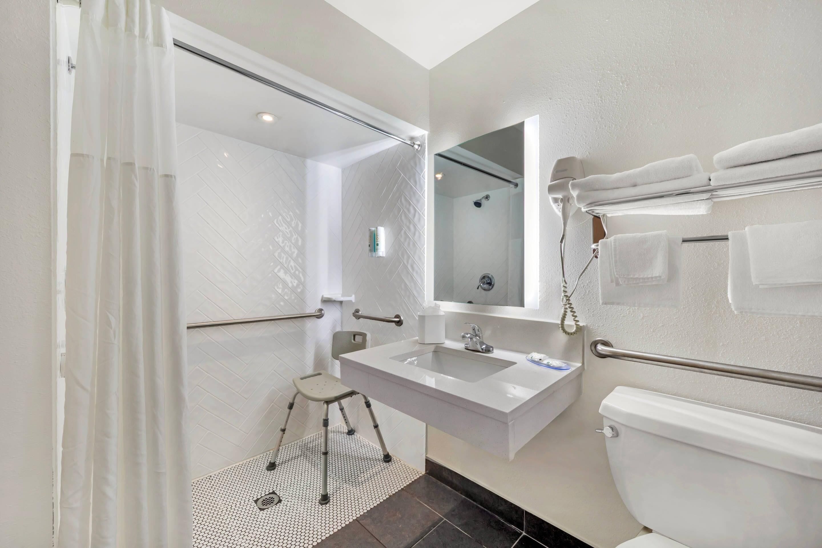 Et moderne badeværelse med bruser, toilet, håndvask og gelændere.