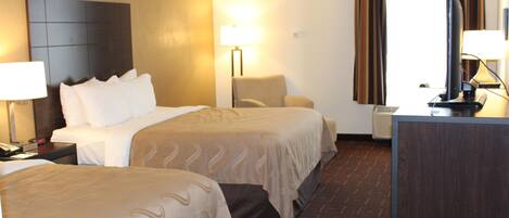 A hotel room with two beds, a desk, a chair, and a TV.