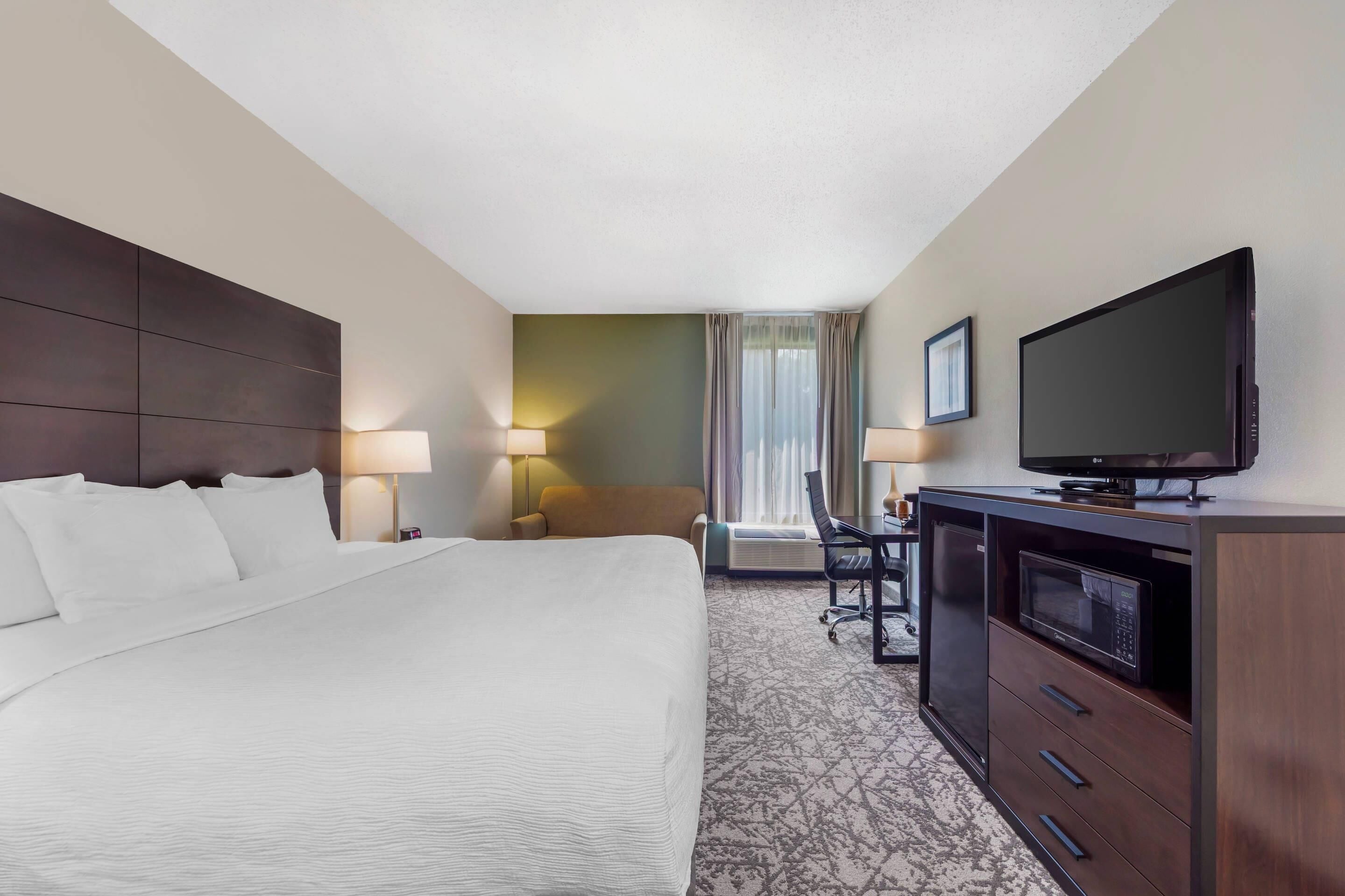 A hotel room with a large bed, a desk with a chair, a television, and a microwave.