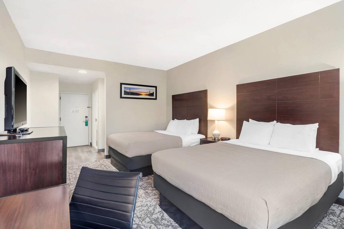 A hotel room with two beds, a desk, a TV, and a framed picture on the wall.