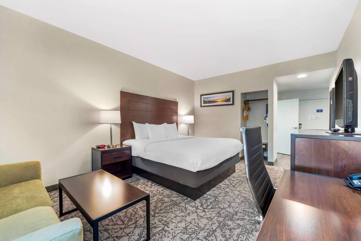 A hotel room with a bed, bedside table, lamp, chair, desk, and a television.