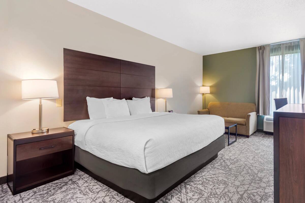 A hotel room with a large bed, two bedside tables with lamps, a sofa, and a desk.