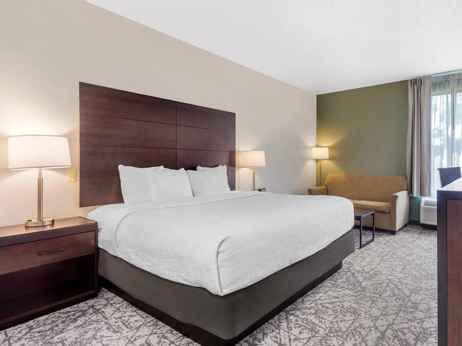 A hotel room with a large bed, two bedside tables with lamps, a sofa, and a desk.