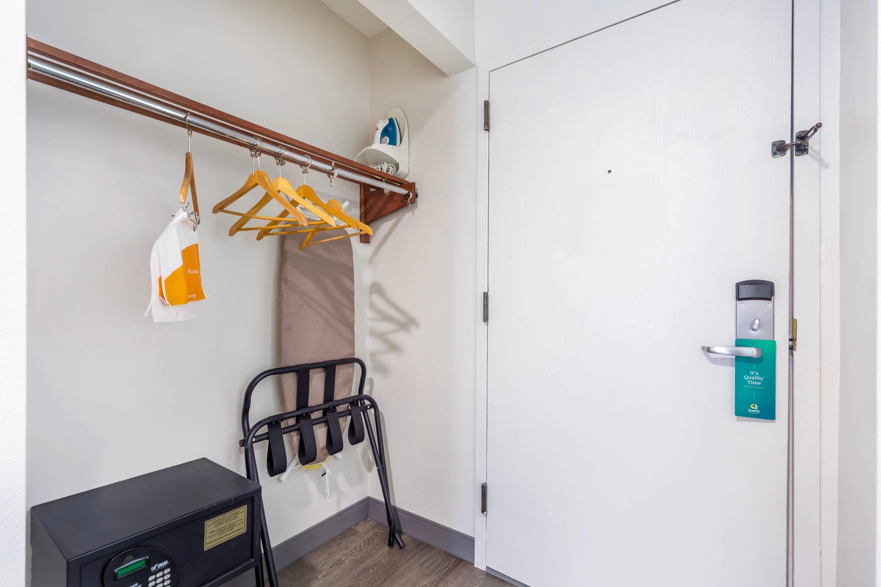 A hotel room with a coat rack, a suitcase, and a door with a keycard reader.